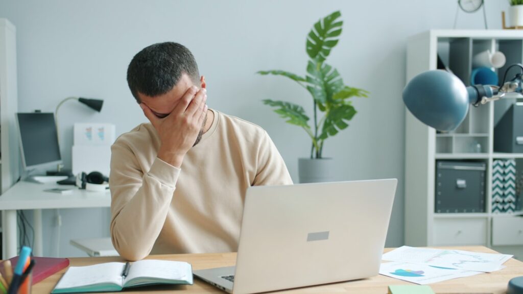 Man rubbing his face in front of laptop.